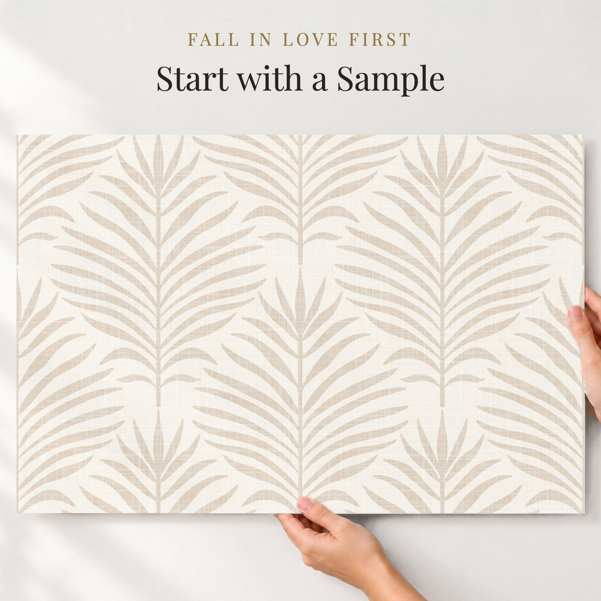 Hands holding a large sample of beige and white Palm Breeze palm leaf wallpaper against a wall
