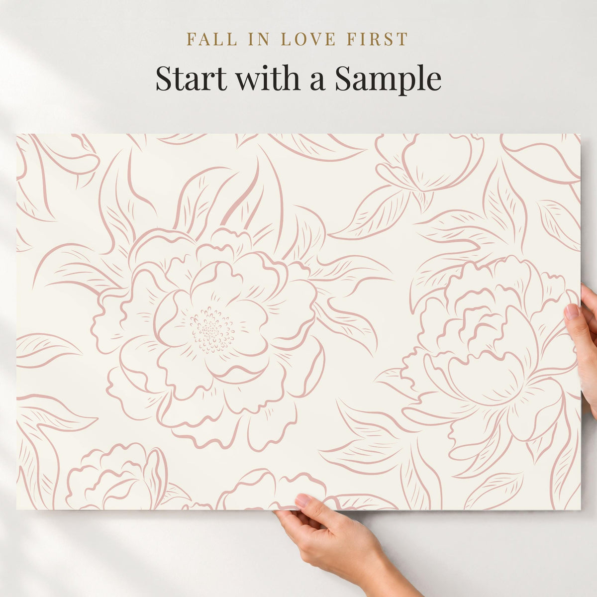 Hands holding a large sample of pink Peony Sketch floral wallpaper against a wall