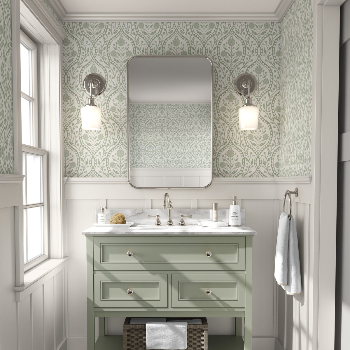 a bathroom with a green vanity and a mirror above it. The walls are covered in a patterned wallpaper, and there are two light fixtures on either side of the mirror. The bathroom appears to be well-lit and organized, with a clean and minimalist design.