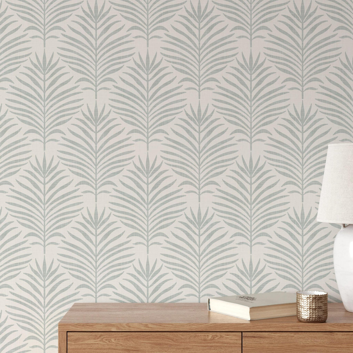 Living room wall of gray green and white Palm Breeze palm leaf wallpaper behind a wood sideboard and lamp