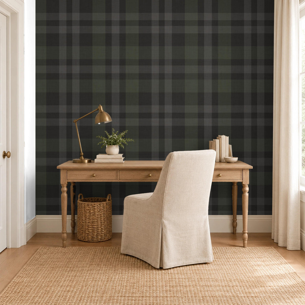 Home office with a wooden desk and upholstered chair against Hollis Plaid wallpaper in charcoal black and olive green