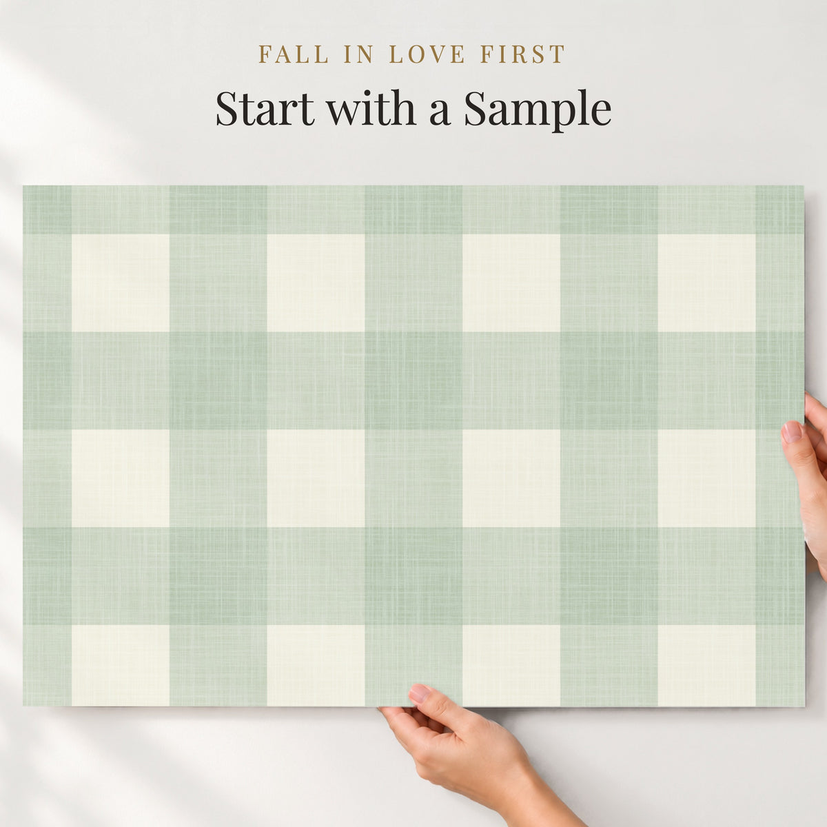 Large sample of sage green gingham wallpaper held up to the wall