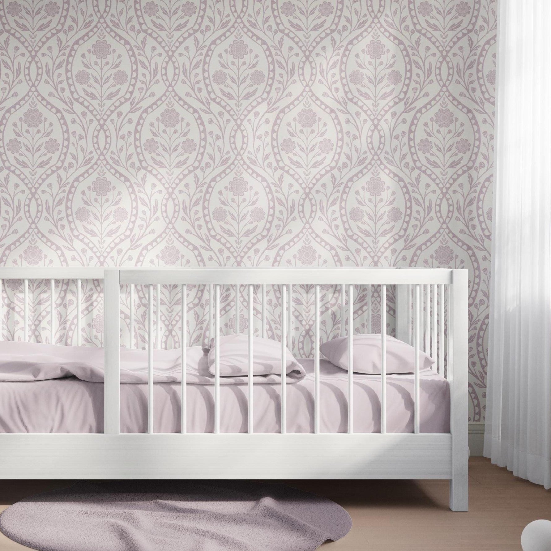 Timeless Baby Girl Nursery Wallpaper in Pastel Purple floral damask on off white background. This elegant wildflower print is shown as Removable Peel & Stick or Prepasted perfect for Victorian, French Country, Cottagecore aesthetics. Featured in girls room as accent wall behind toddler bed.