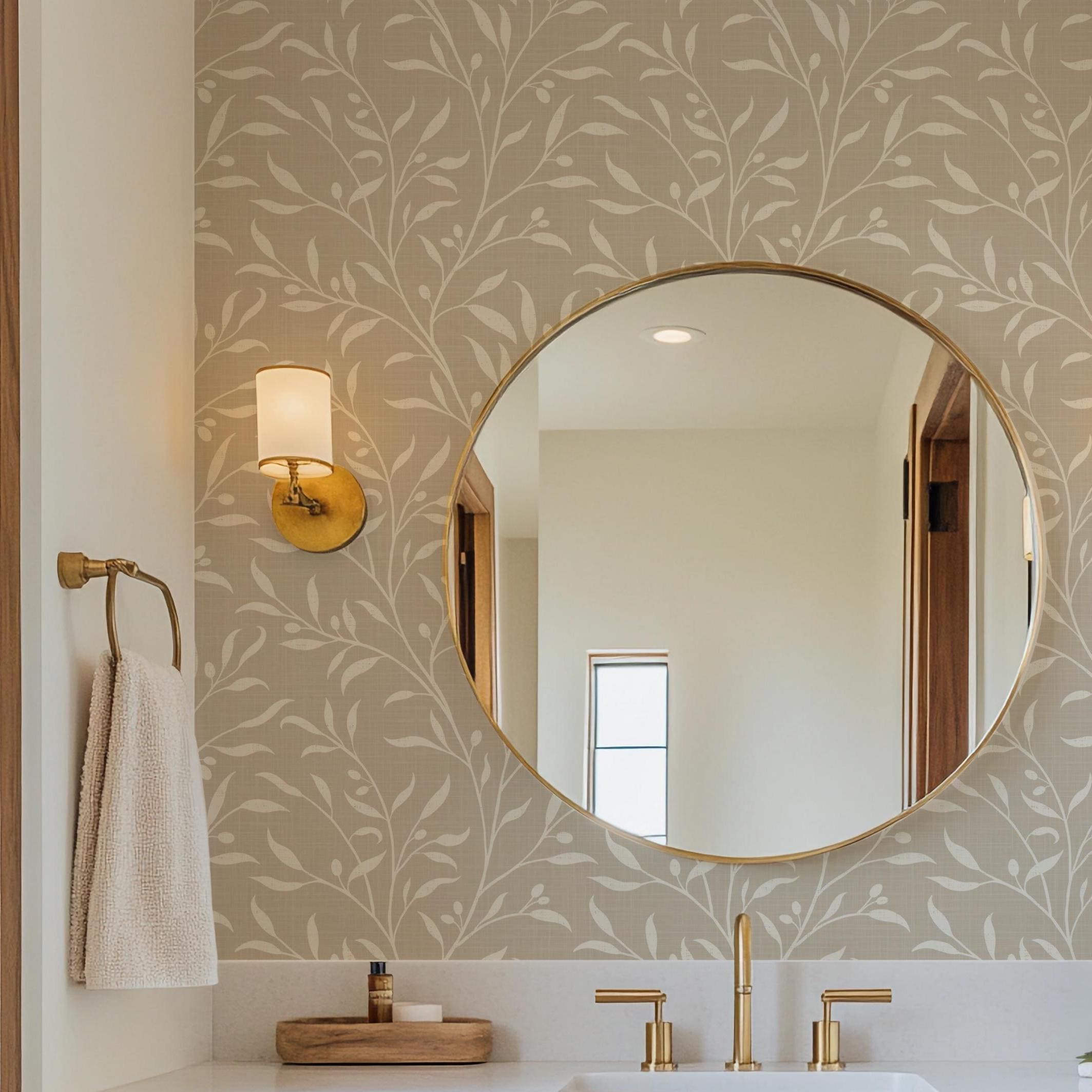 a bathroom with a large round mirror, a wooden countertop, and a gold faucet. The mirror is mounted on the wall above the countertop, which has a sink and a towel rack. The wall behind the mirror has a patterned wallpaper.