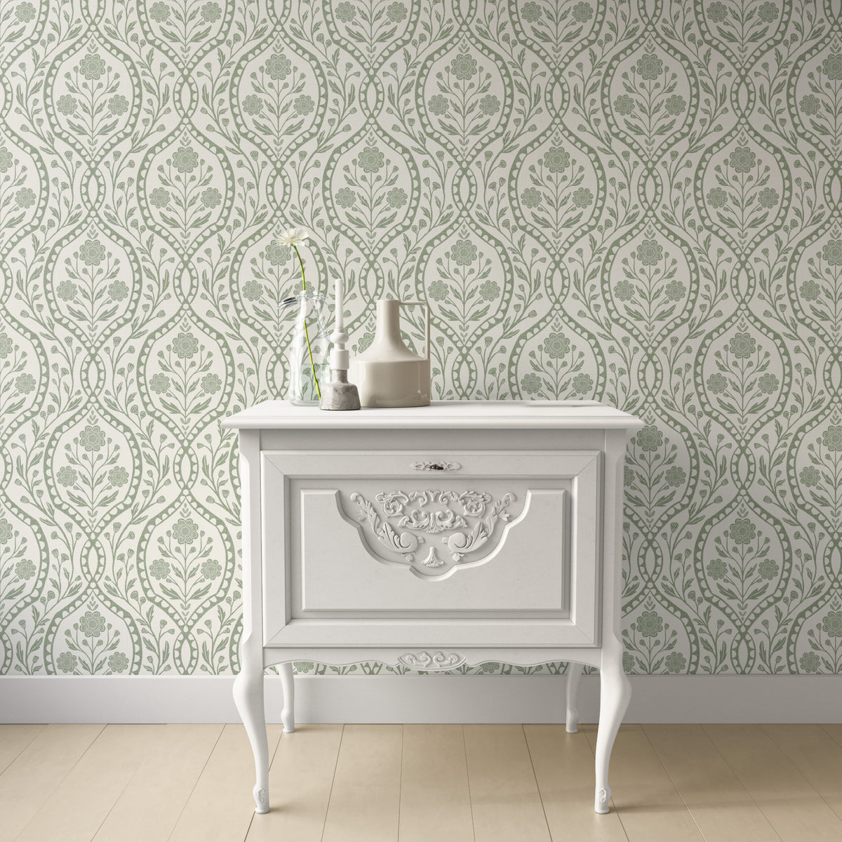 a white wooden dresser with a decorative carved design on the front, set against a patterned wallpaper background.