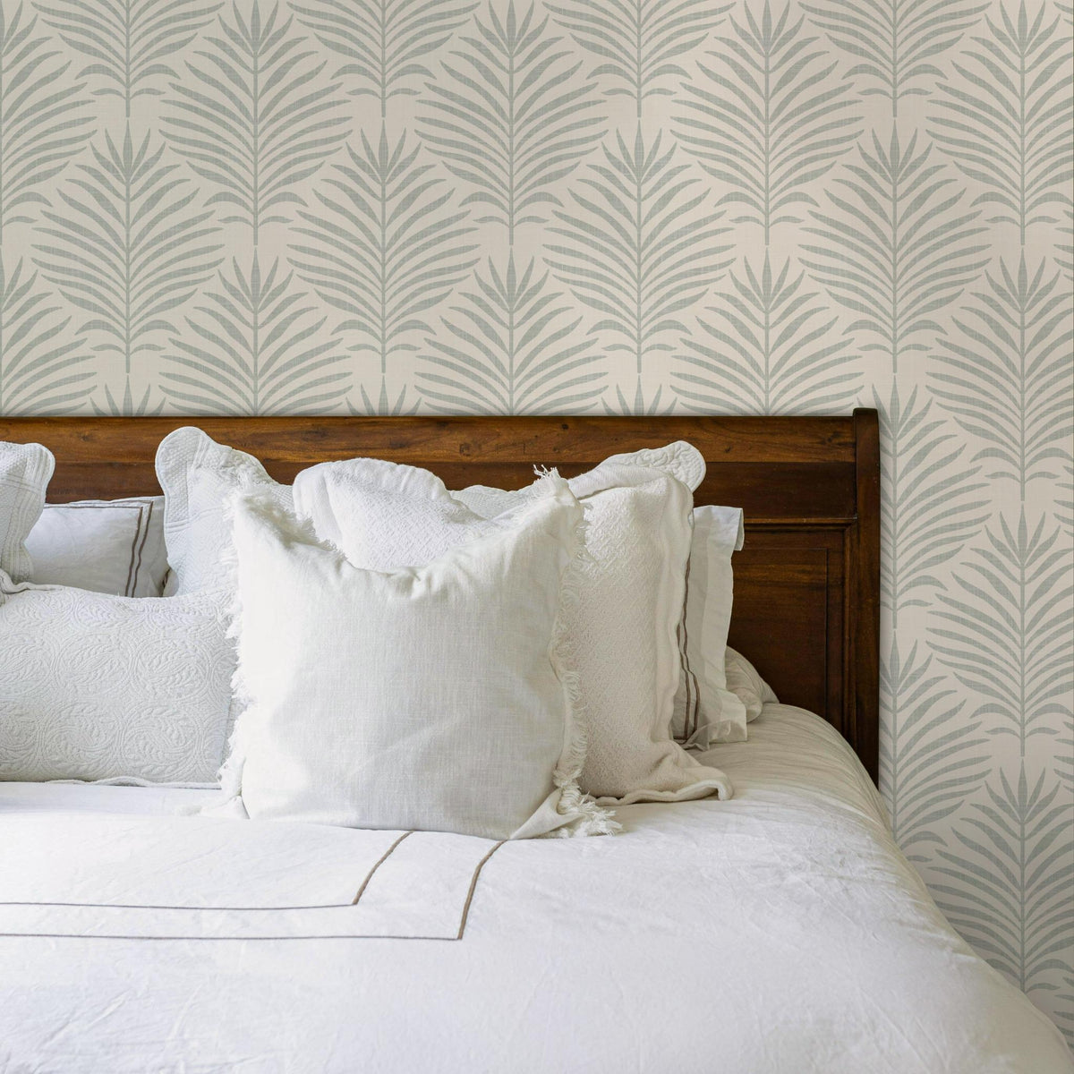 Bedroom with white bedding and a wood headboard against gray green and white Palm Breeze palm leaf wallpaper